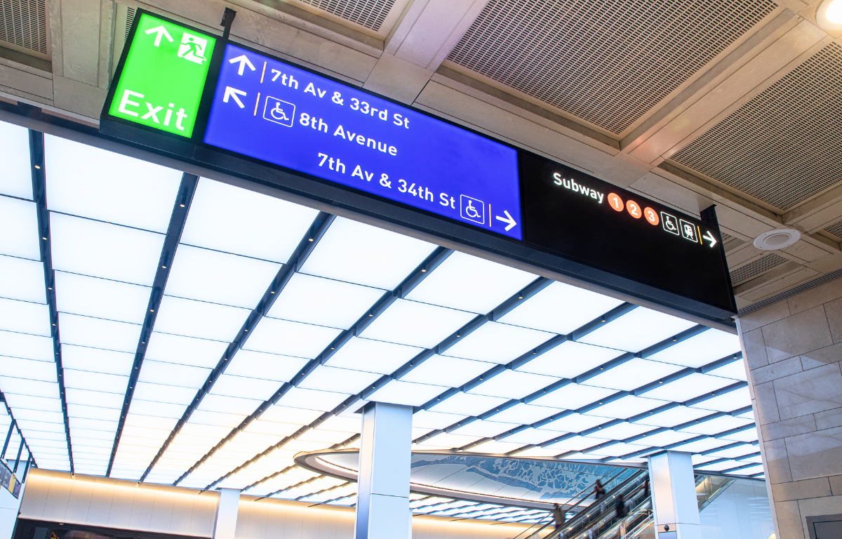 Clear Wayfinding: Accessible Routes at Penn Station An overhead horizontal directional sign at Penn Station indicating exits to 7th Avenue and 8th Avenue. Both exit directions are marked with clear, international symbols for wheelchair accessibility. Adjacent to these are the 1, 2, and 3 subway lines, each accompanied by a wheelchair accessibility icon to indicate barrier-free transit connections.