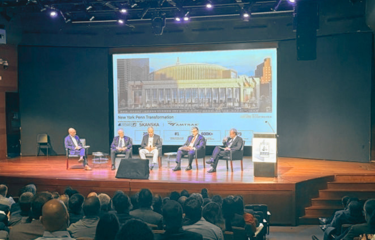 DBIA Blog Post Five panelists sitting on a stage during a presentation at the DBIA NYC Metro Region conference. The projection screen behind them displays a rendering of the New York Penn Station Transformation project.